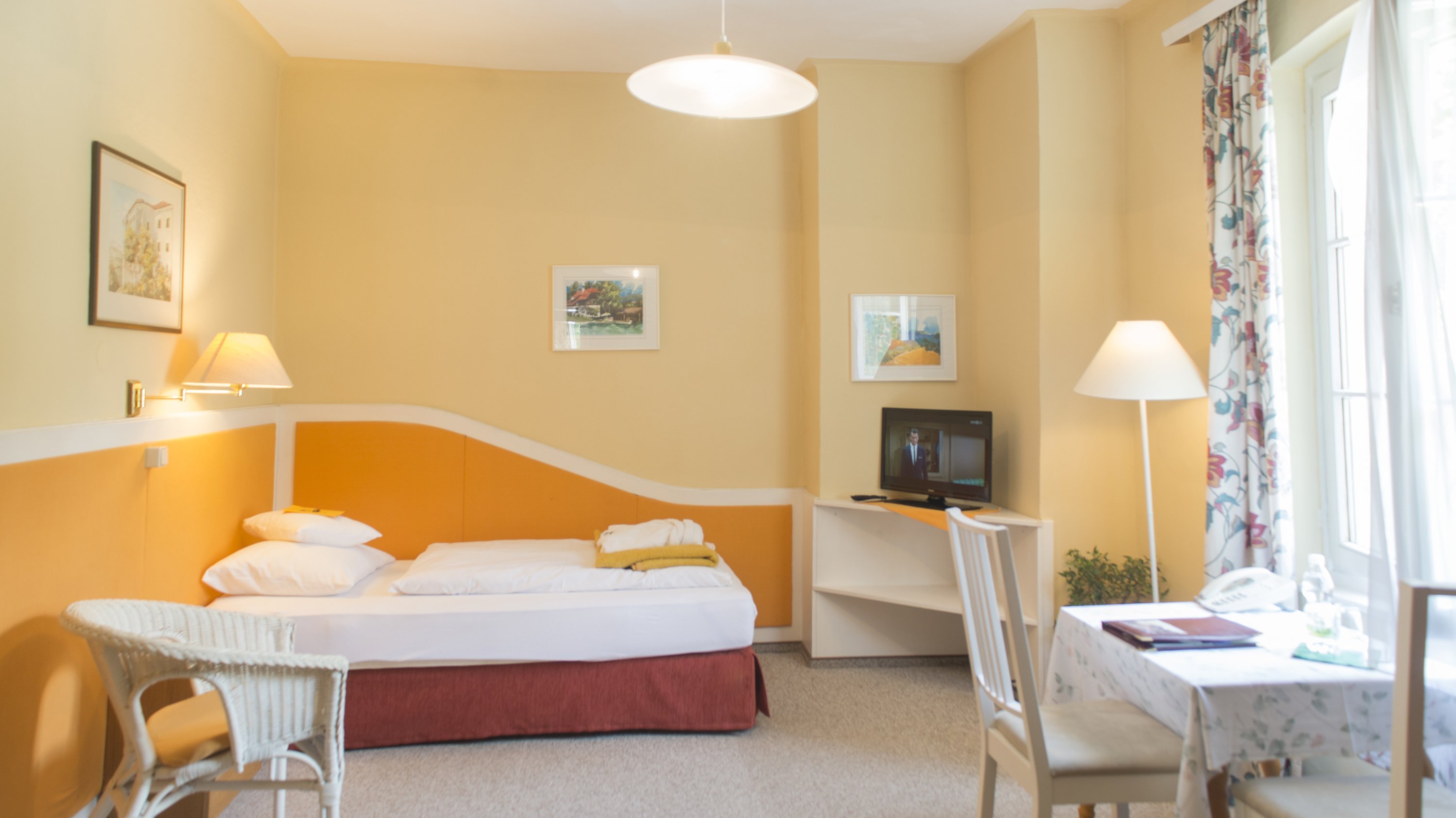 Helle Hotelzimmeratmosphäre Hotelzimmer mit einem Bett, Tisch, Stühlen und Fernseher unter warmen Wänden bei Tageslicht