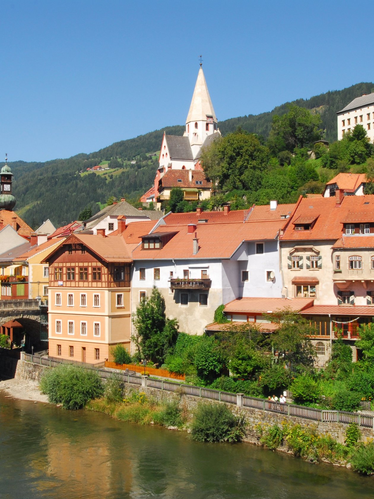 Malersches Dorf am Fluss Ein charmantes Dorf am Ufer eines Flusses mit historischen Gebäuden und Bergen im Hintergrund.