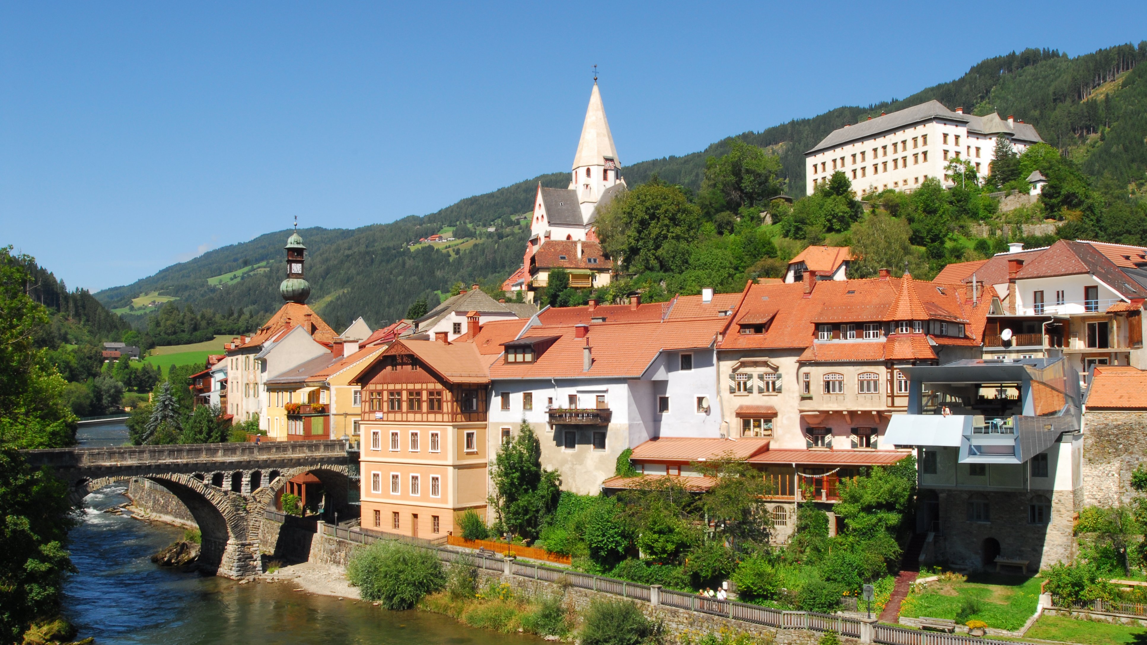Ein charmantes Dorf am Ufer eines Flusses mit historischen Gebäuden und Bergen im Hintergrund.