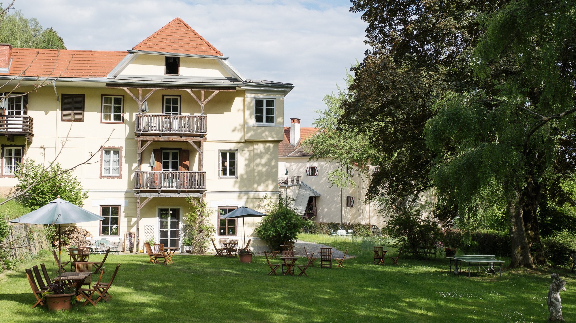 Hotelgebäude mit Sitzgelegenheiten im Freien und Garten umgeben von Bäumen und Grünflächen