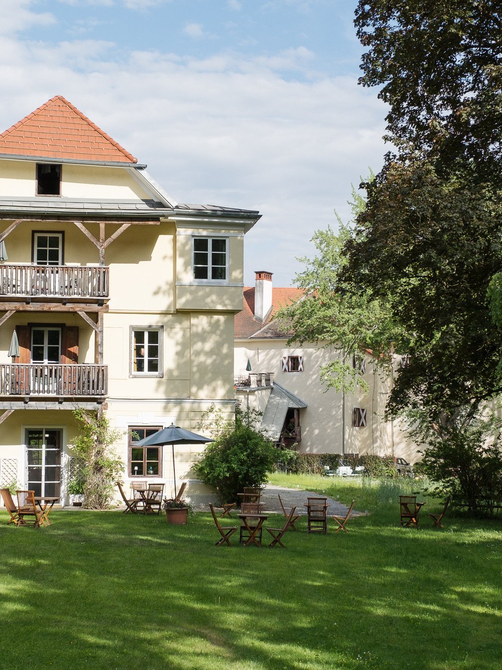 Hotelgebäude mit Sitzgelegenheiten im Freien und Garten umgeben von Bäumen und Grünflächen