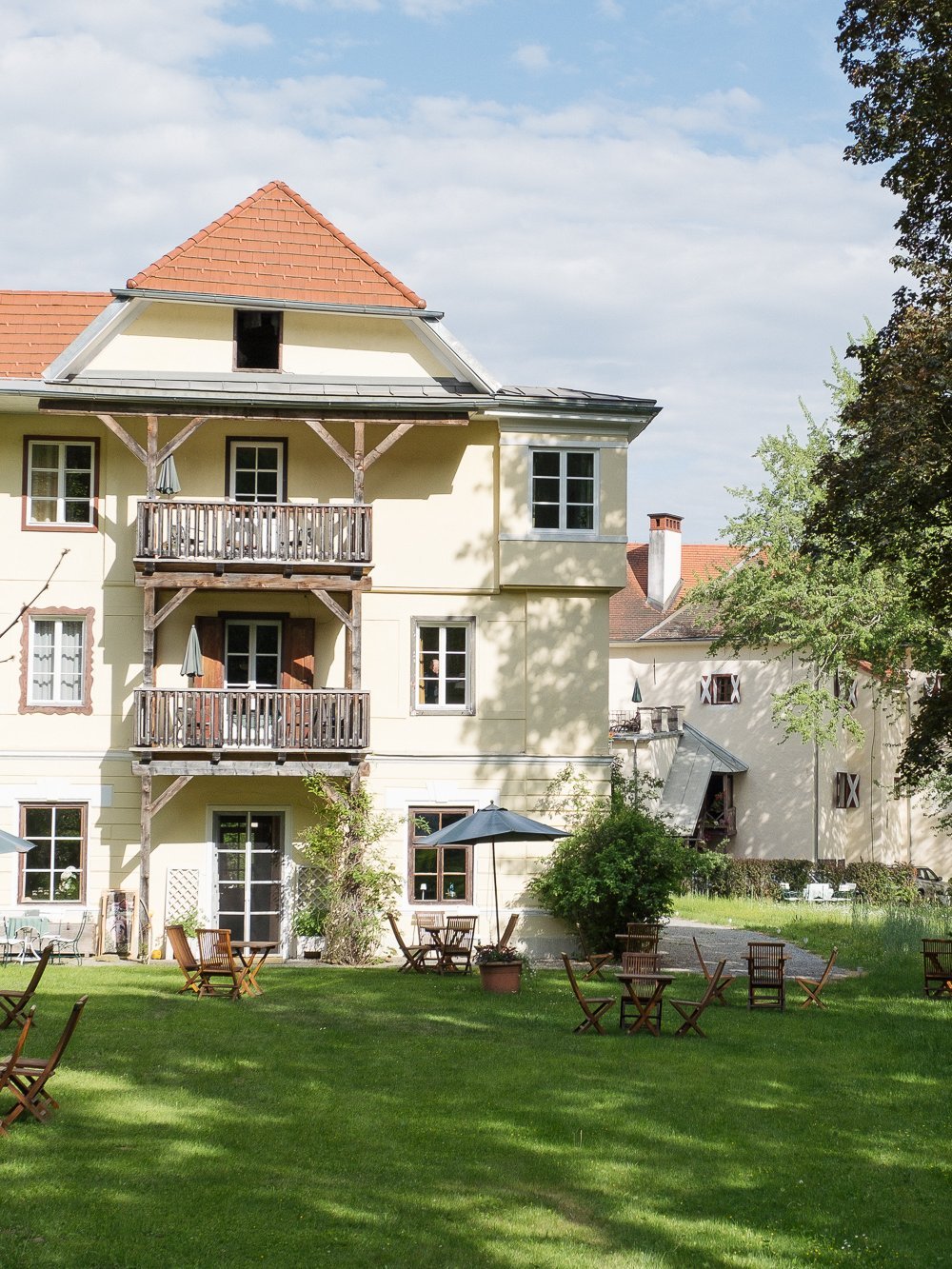 Idyllisches Hotel im Grünen Hotelgebäude mit Sitzgelegenheiten im Freien und Garten umgeben von Bäumen und Grünflächen