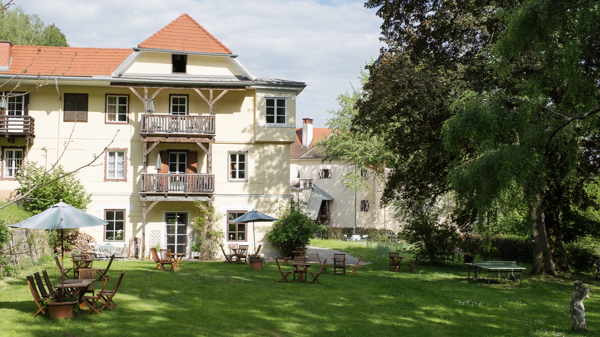 Idyllisches Hotel im Grünen Hotelgebäude mit Sitzgelegenheiten im Freien und Garten umgeben von Bäumen und Grünflächen