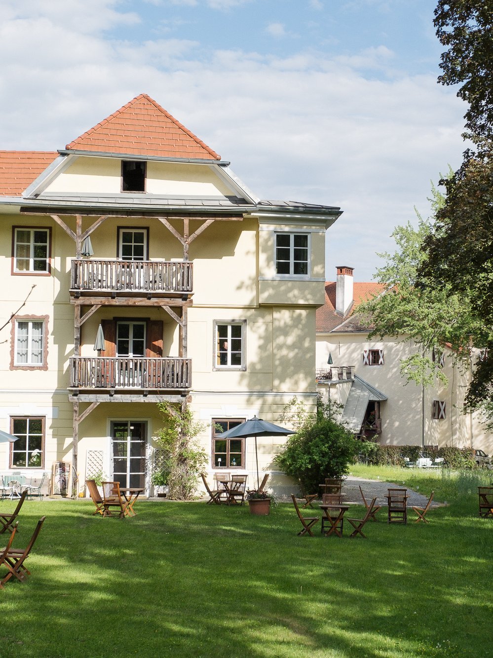Outdoor Relaxation at Pischlschloss A hotel building with balconies surrounded by green garden and outdoor seating areas