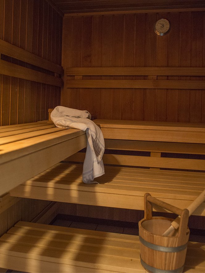 Entspannung in der Sauna Inneneinrichtung einer hölzernen Sauna mit Bänken, einem Handtuch und einem Holzbehälter mit Schöpflöffel.