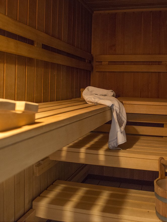 Entspannung in der Sauna Inneneinrichtung einer hölzernen Sauna mit Bänken, einem Handtuch und einem Holzbehälter mit Schöpflöffel.