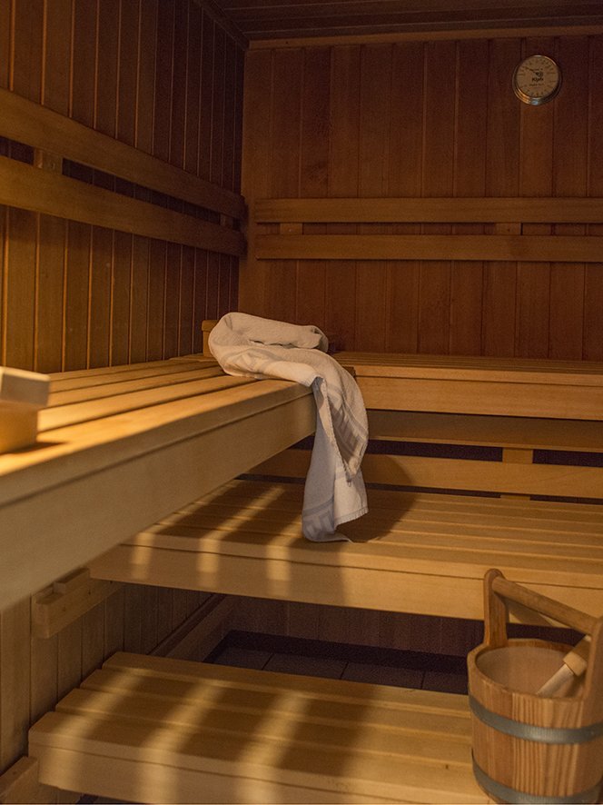 Entspannung in der Sauna Inneneinrichtung einer hölzernen Sauna mit Bänken, einem Handtuch und einem Holzbehälter mit Schöpflöffel.