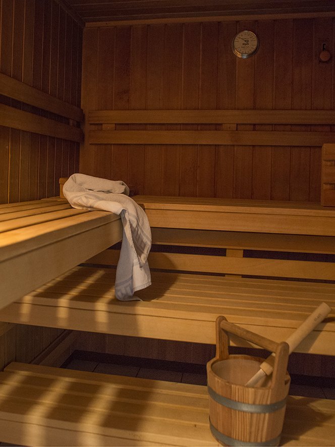 Inneneinrichtung einer hölzernen Sauna mit Bänken, einem Handtuch und einem Holzbehälter mit Schöpflöffel.