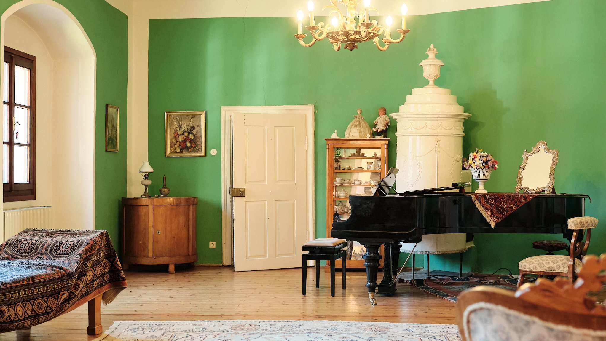 Elegante Atmosphäre im Salon Salon mit grünen Wänden, einem Klavier und vintage Möbeln, beleuchtet von einem Kronleuchter