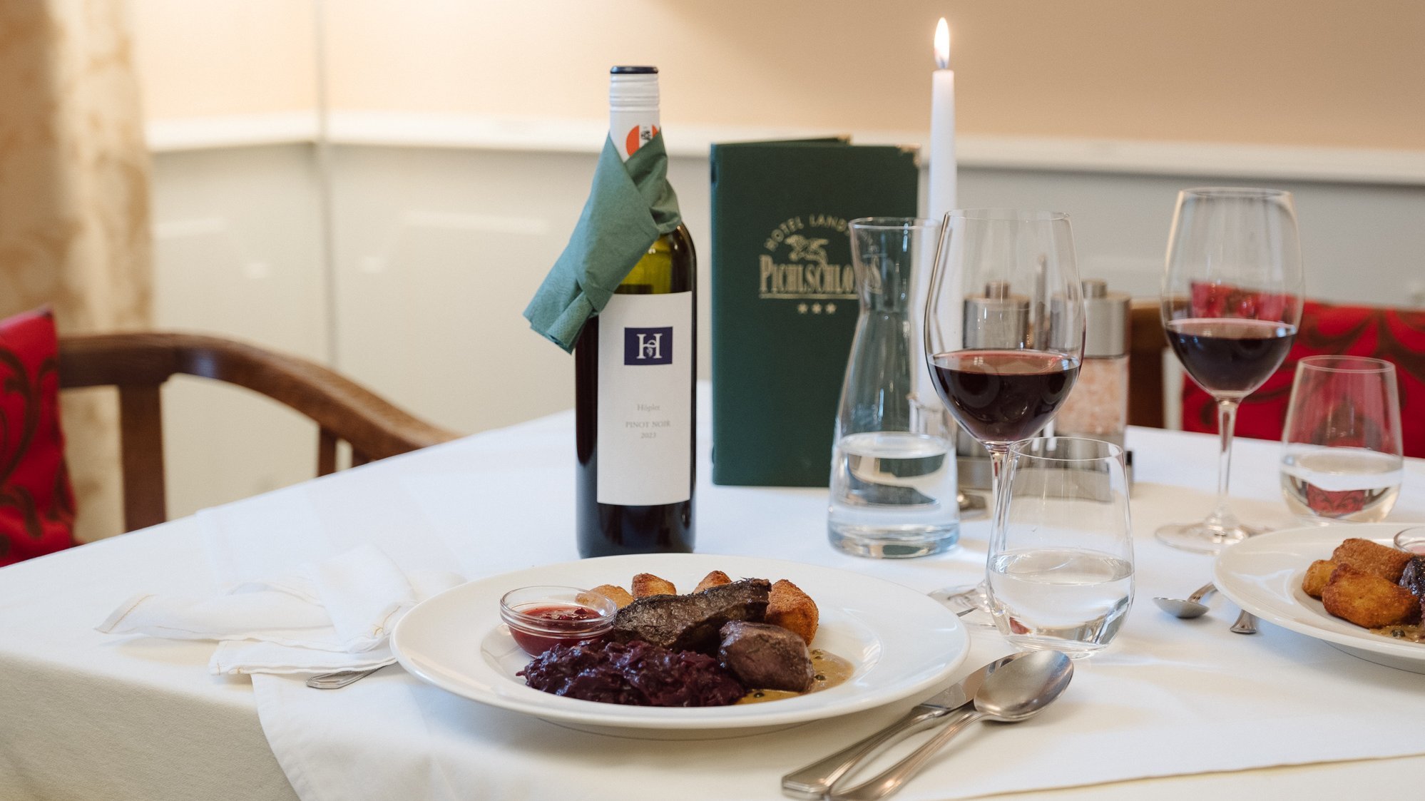 Elegantes Tischgedeck für Gourmet-Erlebnis Tisch mit gedecktem Geschirr, einer Flasche Rotwein und Gläsern in feinem Restaurantambiente