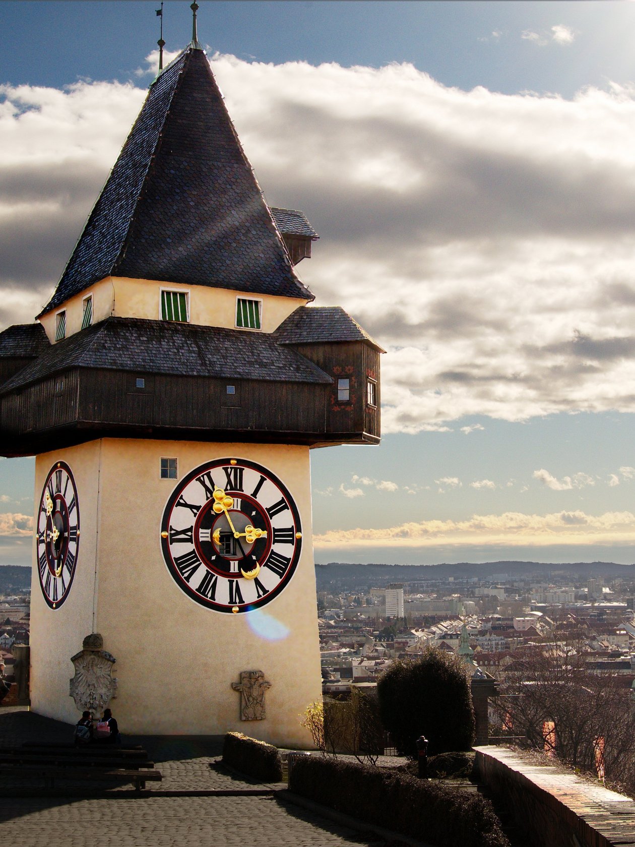 Uhrturm in Graz Architektonischer Uhrturm auf einem Hügel über der Stadt Graz mit Wolken im Hintergrund