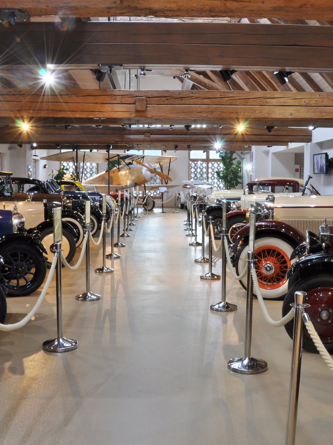Ein Raum mit Oldtimern unter Holzbalken in einem Automobilmuseum. Vintage Fahrzeuge sind aufgereiht.