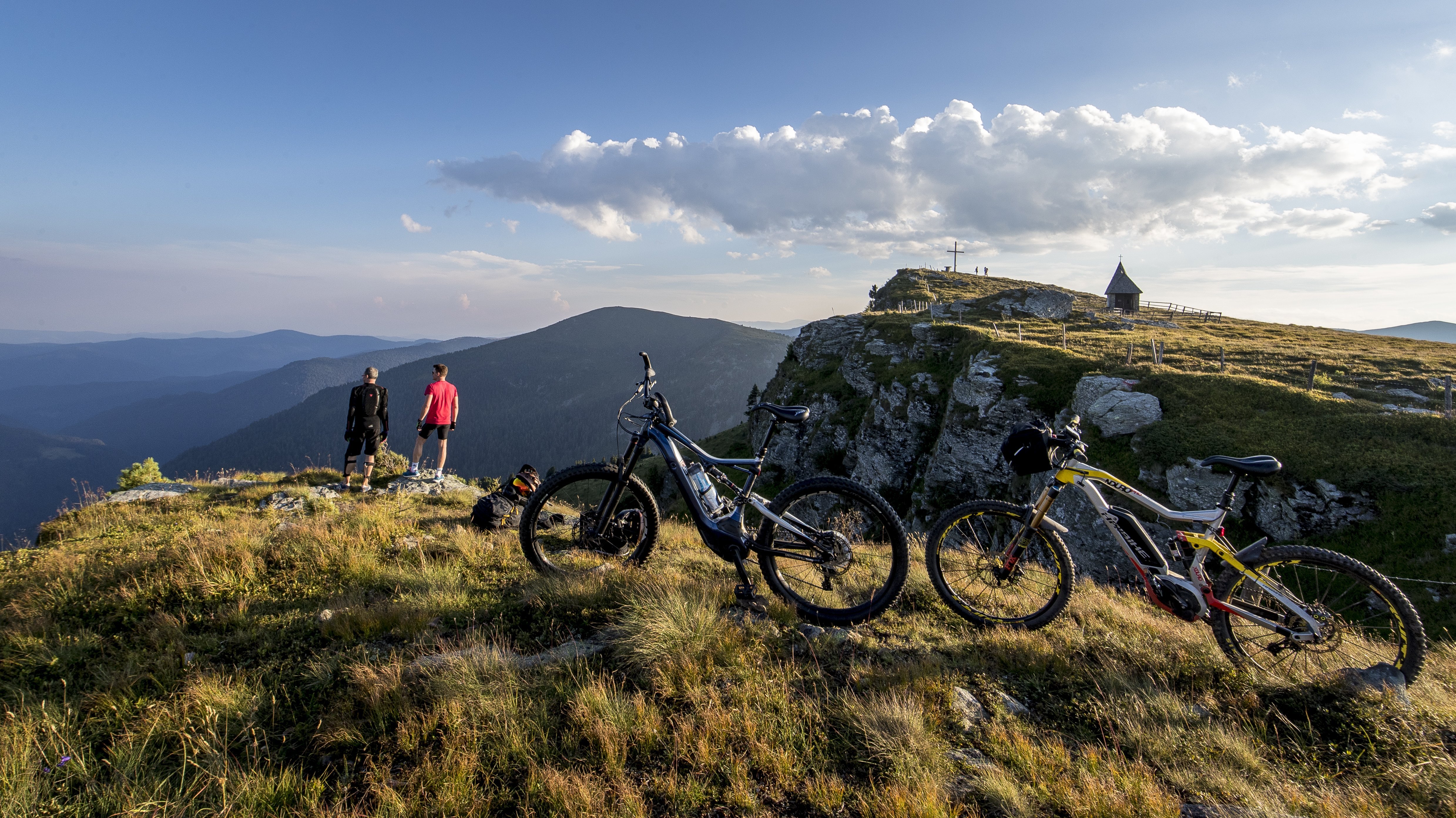Abenteuer auf dem Berg Zwei Personen mit Fahrrädern stehen auf einem Gipfel und blicken über eine weite Landschaft.