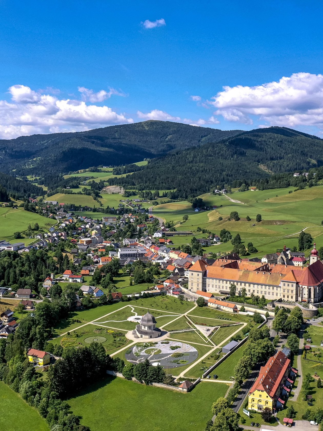 Luftaufnahme eines historischen Gebäudes umgeben von grünen Feldern und Bergen in einer malerischen Landschaft