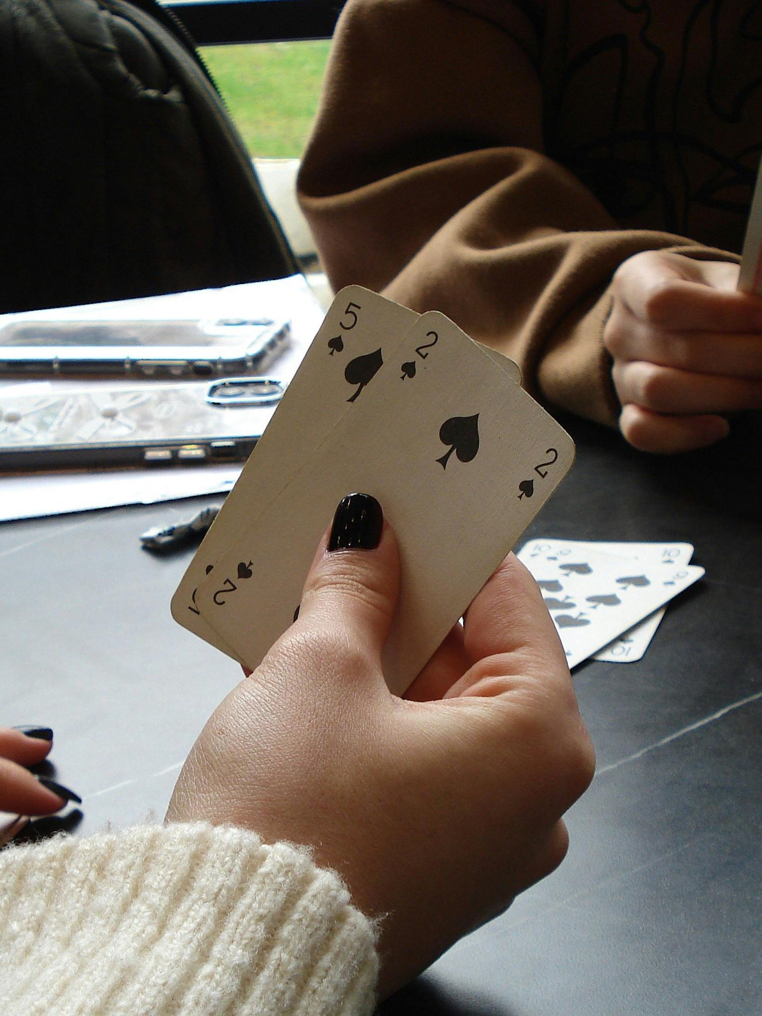 Gesellige Spielrunde am Tisch Eine Gruppe von Personen spielt Karten an einem Tisch, Hände mit Karten sind sichtbar.