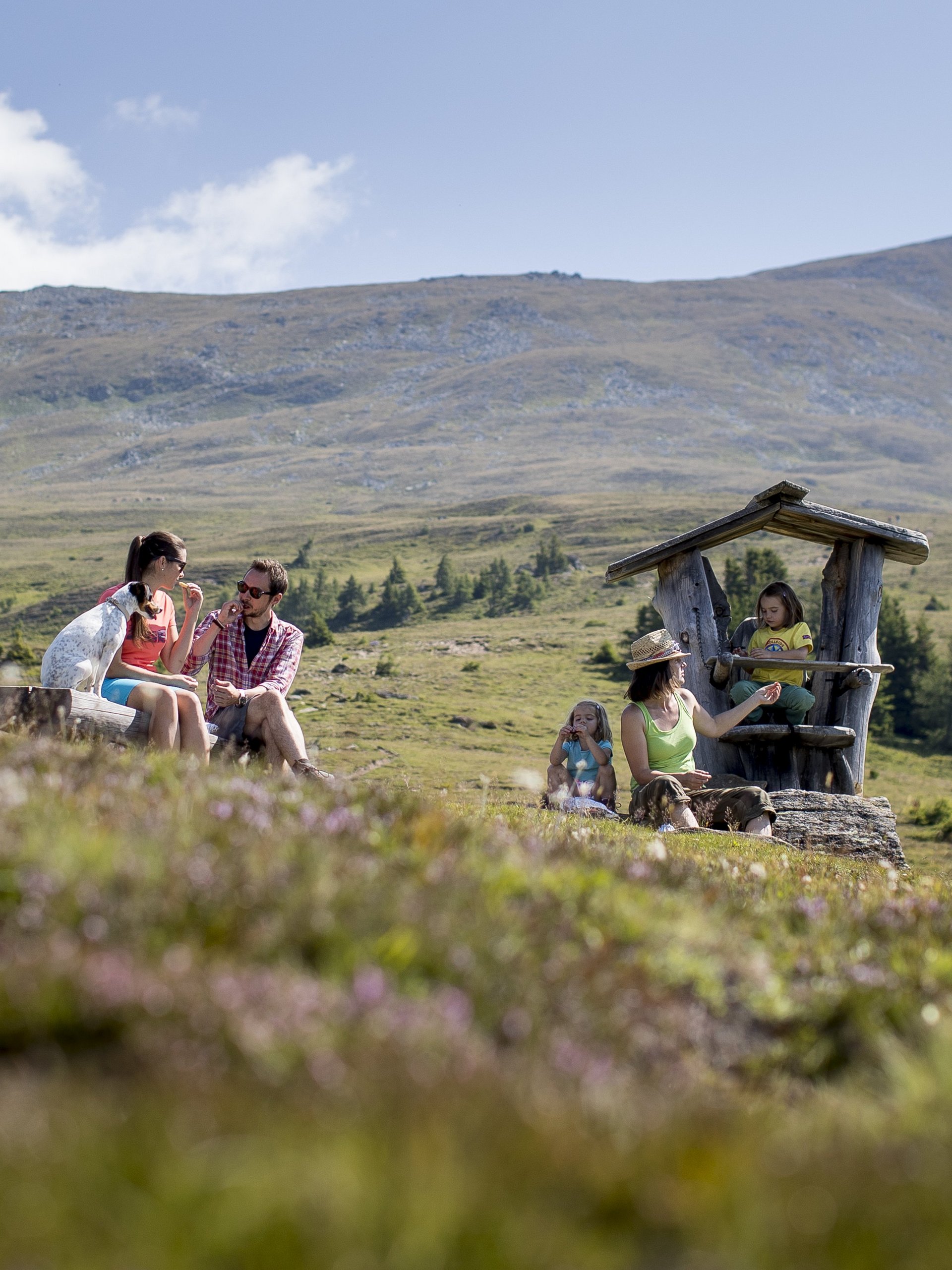 Gruppe von Menschen genießt ein Picknick in einer bergigen Umgebung mit viel Grün und blauem Himmel.