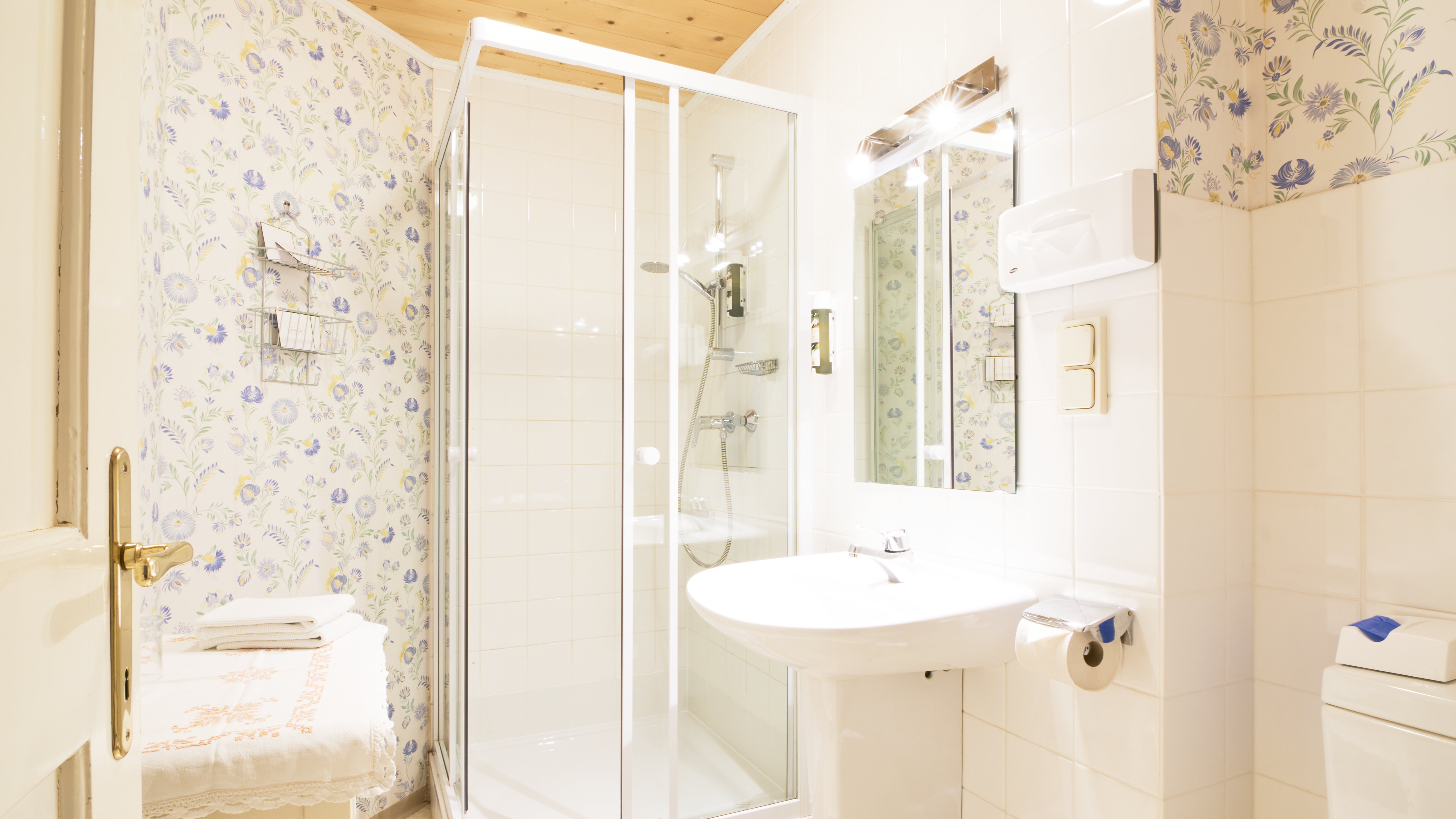Helle Badezimmeratmosphäre im Pichlschloss Badezimmer mit Dusche, Waschbecken und floralen Tapeten in einem stilvollen Raum
