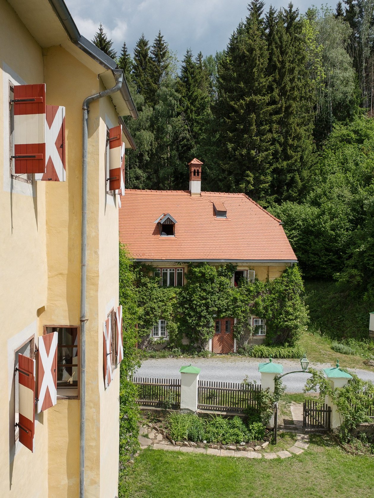 Das Hotel Landsitz Pichlschloss mit roten und weißen Fensterläden, umgeben von Grünanlagen und einem gepflegten Garten
