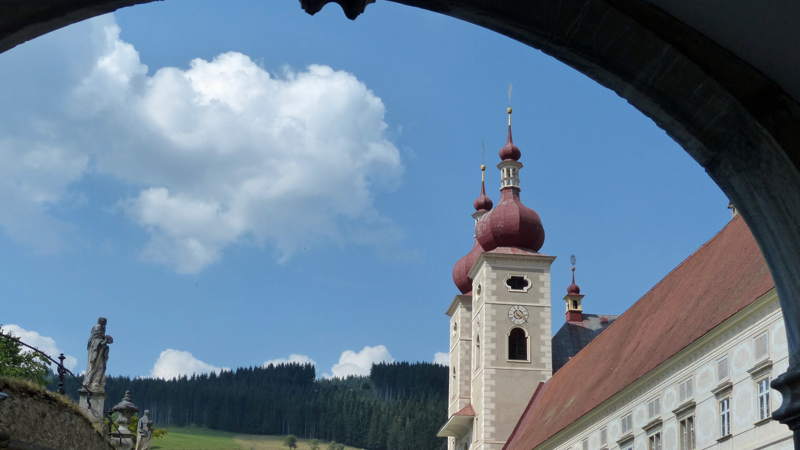 Historisches Kloster mit roten Kuppeln Ein historisches Kloster mit roten Kuppeln vor grünen Bergen unter einem teils bewölkten Himmel