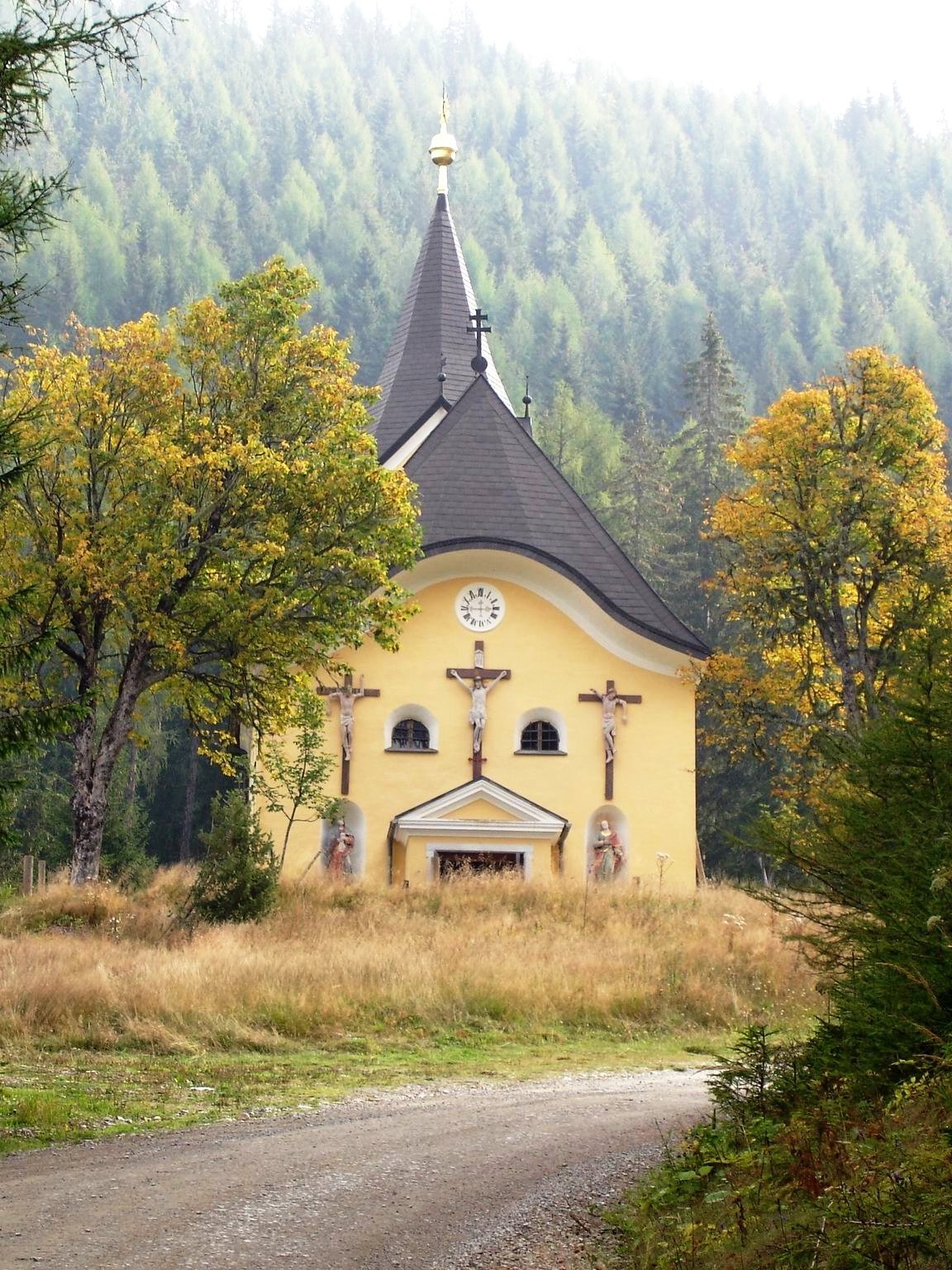 Herbstliche Kirschenszene Gelbe Kirche umgeben von Bäumen in einem Wald während des Herbstes, grüne Blätter und fallende Blätter sind sichtbar