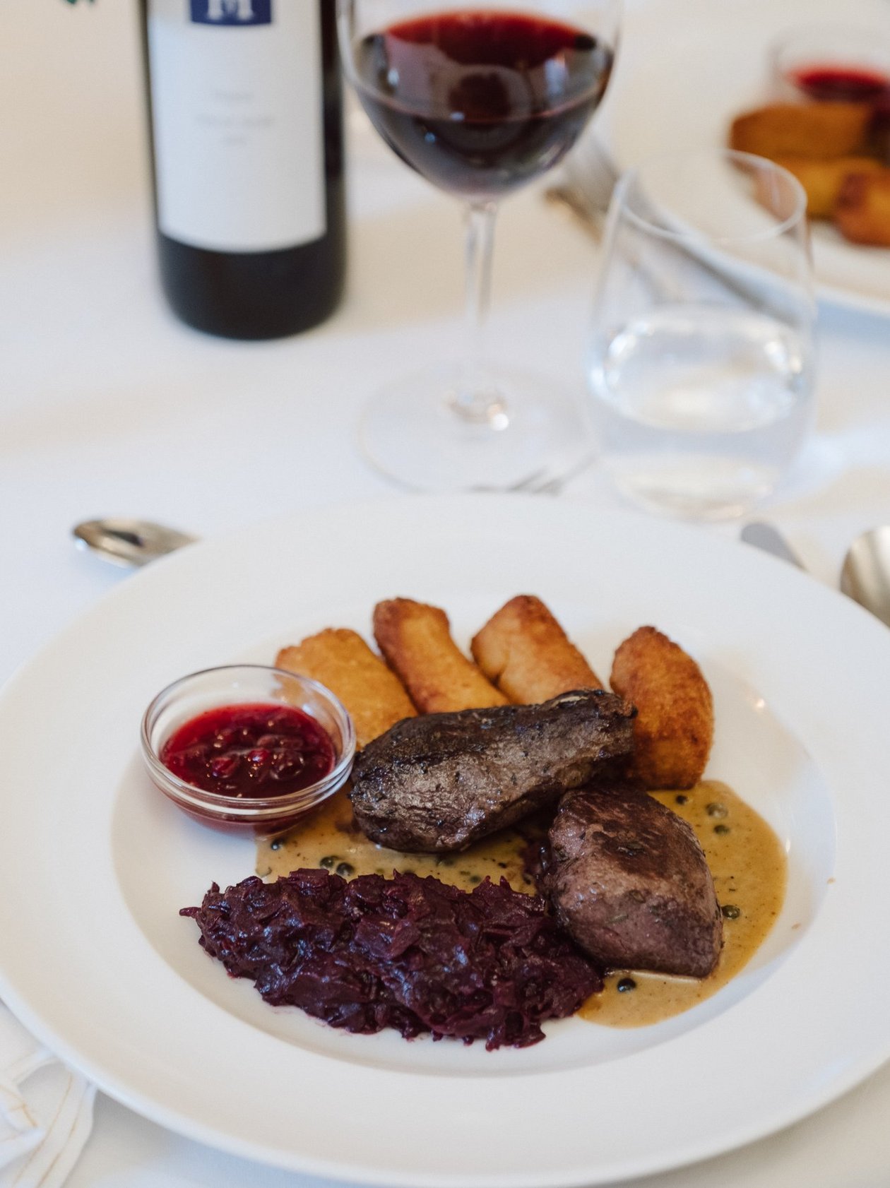 Kulinarische Freude mit feinem Rindfleisch Gourmetgericht mit Rindfleisch, Rotkohl, Bratkartoffeln und Rotwein in Gläsern serviert