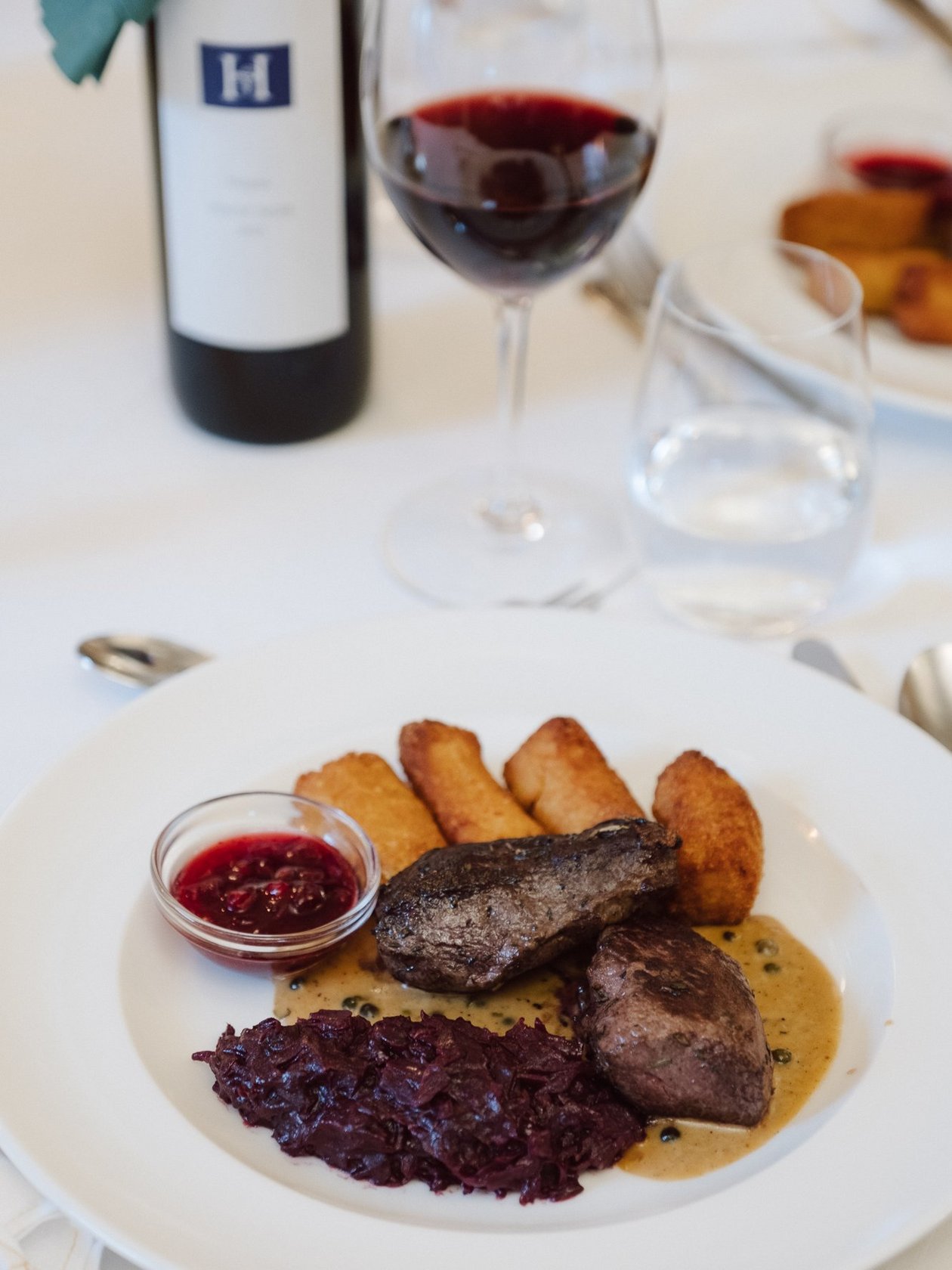 Kulinarische Freude mit feinem Rindfleisch Gourmetgericht mit Rindfleisch, Rotkohl, Bratkartoffeln und Rotwein in Gläsern serviert