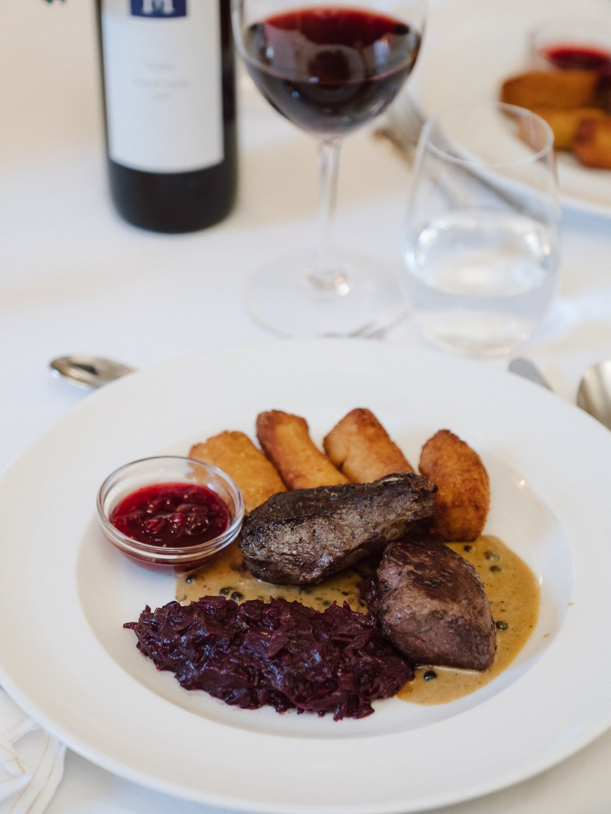 Gourmet Beef Dish with Red Wine A beautifully plated gourmet beef dish with red cabbage, sauce, and side items paired with glasses of red wine