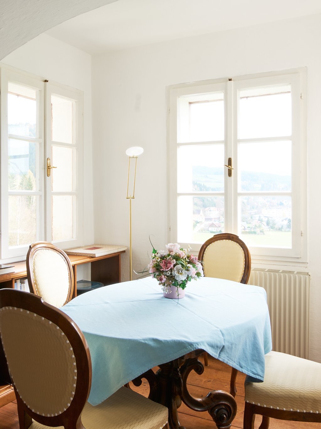 Dynamisches Esszimmer mit einem Tisch und Stühlen, erhellt von großen Fenstern, dekoriert mit blauer Tischdecke.