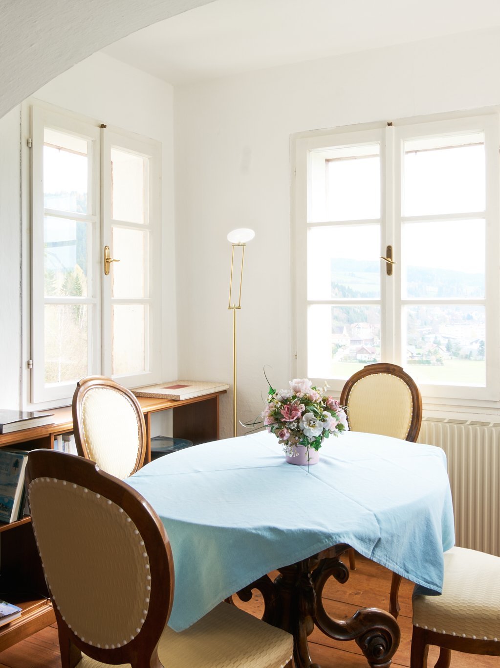 Dynamisches Esszimmer mit einem Tisch und Stühlen, erhellt von großen Fenstern, dekoriert mit blauer Tischdecke.