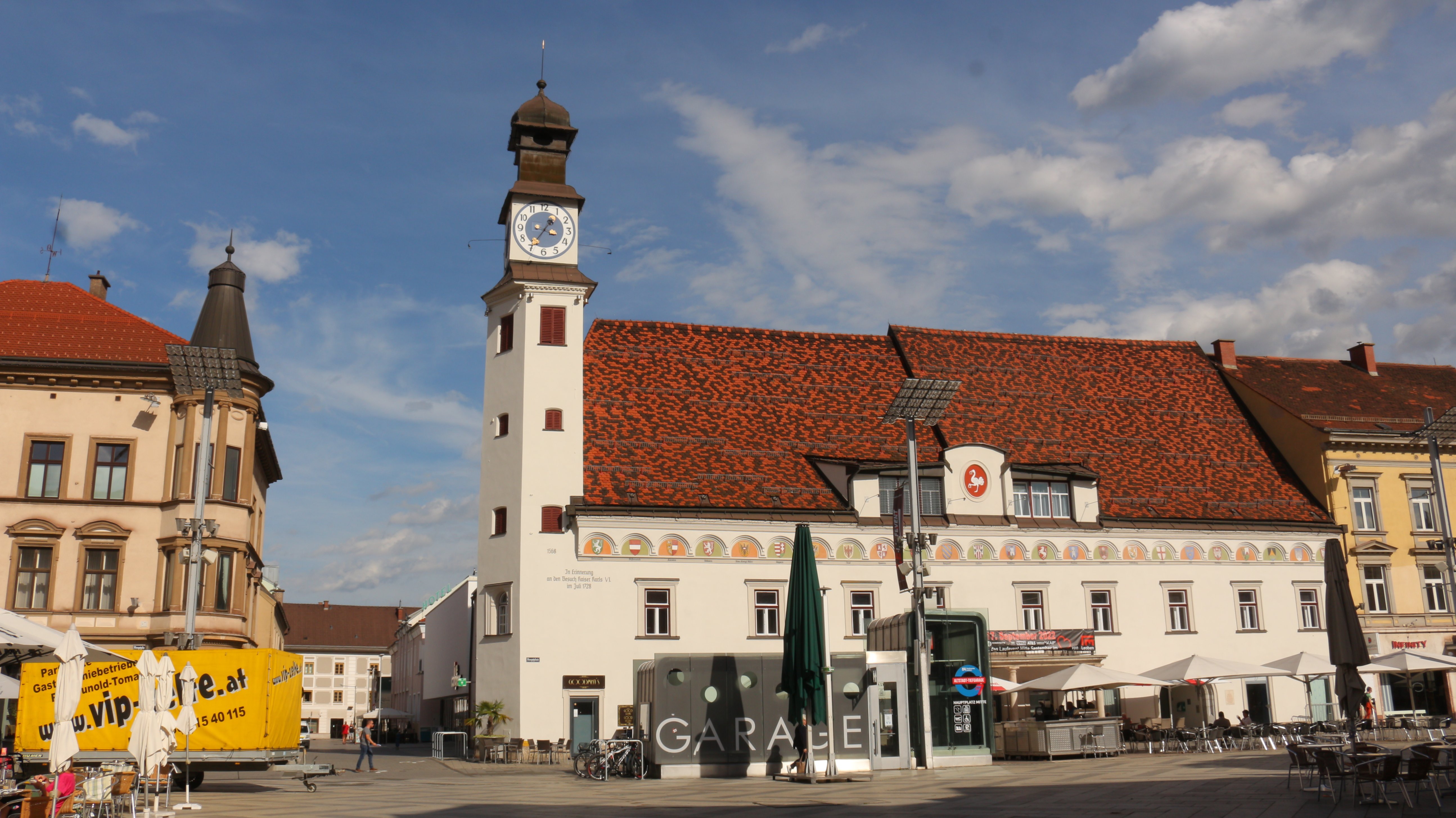 Stadtplatz mit historischem Gebäude, das einen Uhrturm und Außenbestuhlung zeigt.