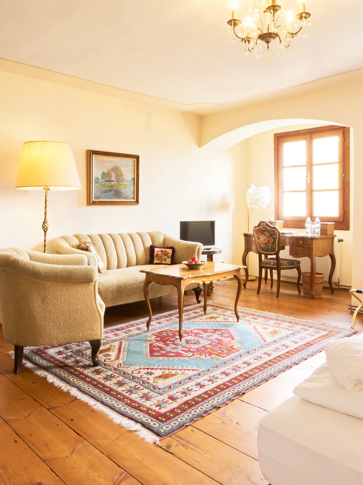 Elegante Zimmergestaltung im Hotel Landsitz Pischlschloss Behagliches Hotelzimmer mit Sofa, Tisch und Bett in weißer Bettwäsche sowie angrenzendem Badezimmer.