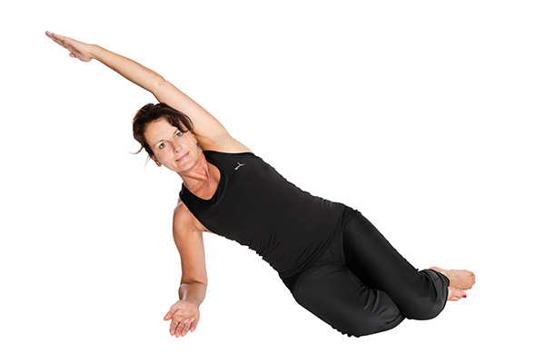 Claudia Novak bei einer Yoga-Übung - in Seitenlage, wobei der linke Arm in die Höhe gestreckt wird.