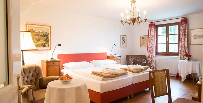 Blick in das Schlosszimmer - Doppelbett, Schreibtisch mit Stuhl und kleiner runder Tisch mit Lehnsessel.