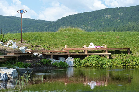 Person liegt am Steg bei der Naturleseinsel Zeutschacher Ursprungsquelle